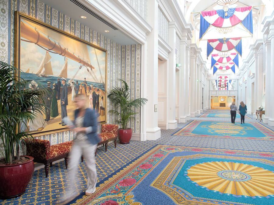 A grand hotel lobby with a large nautical-themed mural, ornate columns, and a patterned carpet.