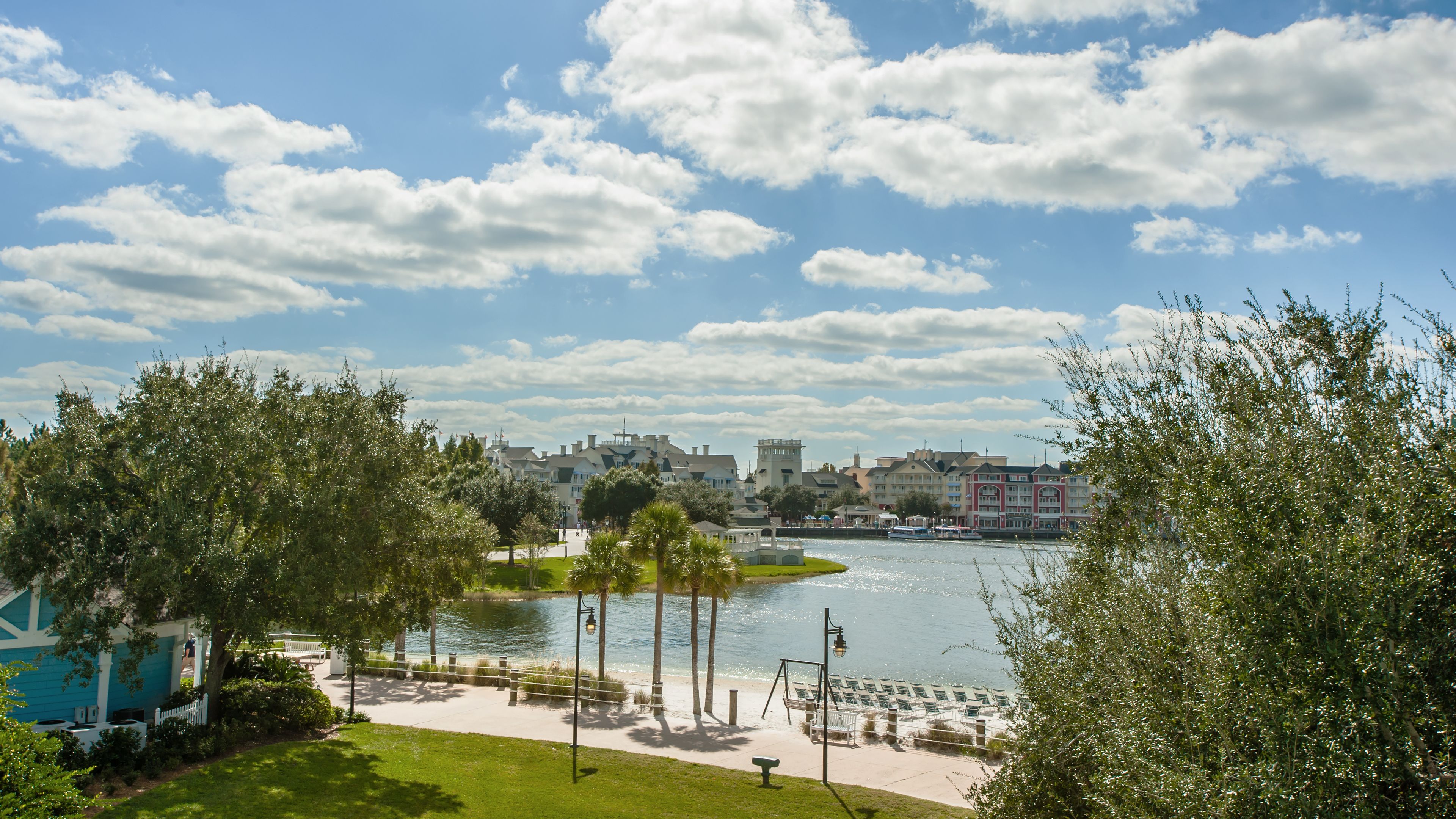 A lakeside park with a walking path, benches, and a view of buildings across the water.