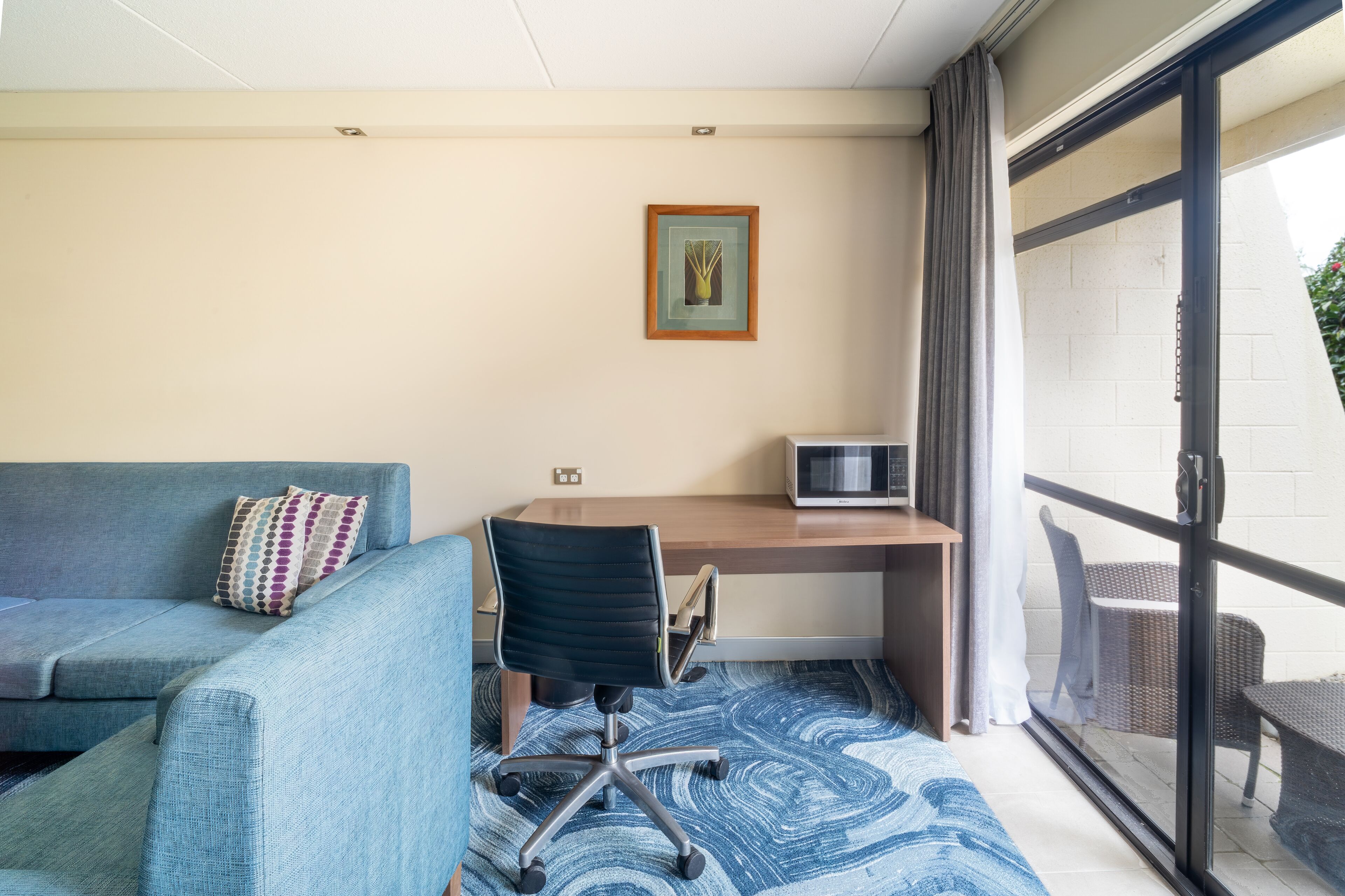 A room with a blue sofa, a wooden desk with a laptop, a chair, and a patterned rug.