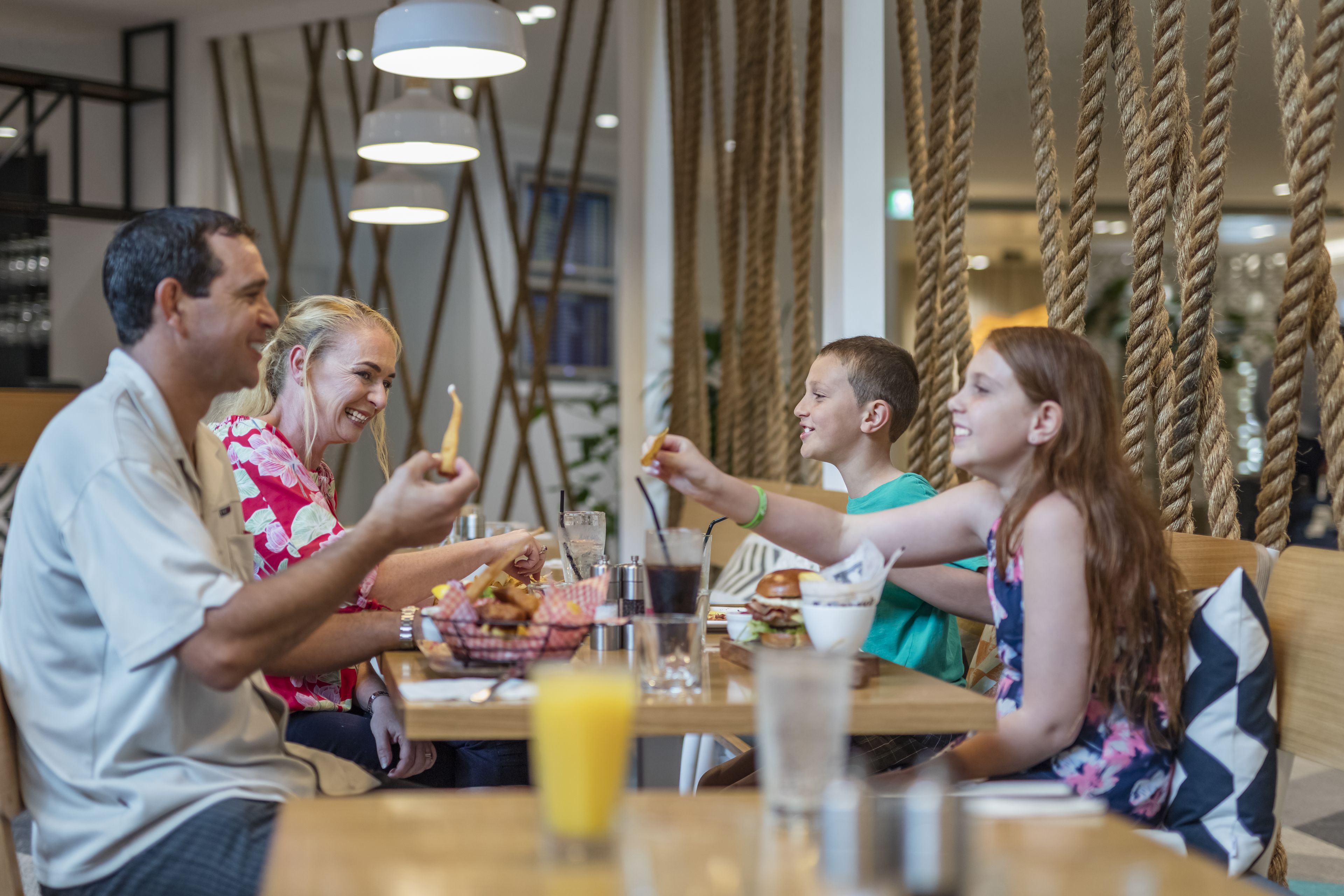 A group of people dining at a restaurant with a casual setting, featuring a wooden table and hanging ropes as decor.