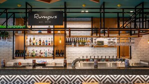 A bar area with a sign reading 'Rumpus est. 2018', shelves with bottles, a bar counter, and a patterned wall. - Holiday Inn Auckland Airport by IHG (Auckland)