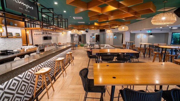 A modern restaurant interior with a bar area, wooden tables, and black chairs. - Holiday Inn Auckland Airport by IHG (Auckland)