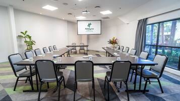 A conference room with a large table, chairs, a projector screen, and a view of trees through a window.