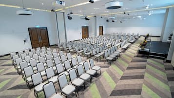Ett konferensrum med rader av stolar, en scen med ett talarstånd och projektorer som är monterade i taket.