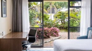 A hotel room with a bed, a desk, a chair, and a view of a garden through a glass door. - Holiday Inn Auckland Airport by IHG (Auckland)