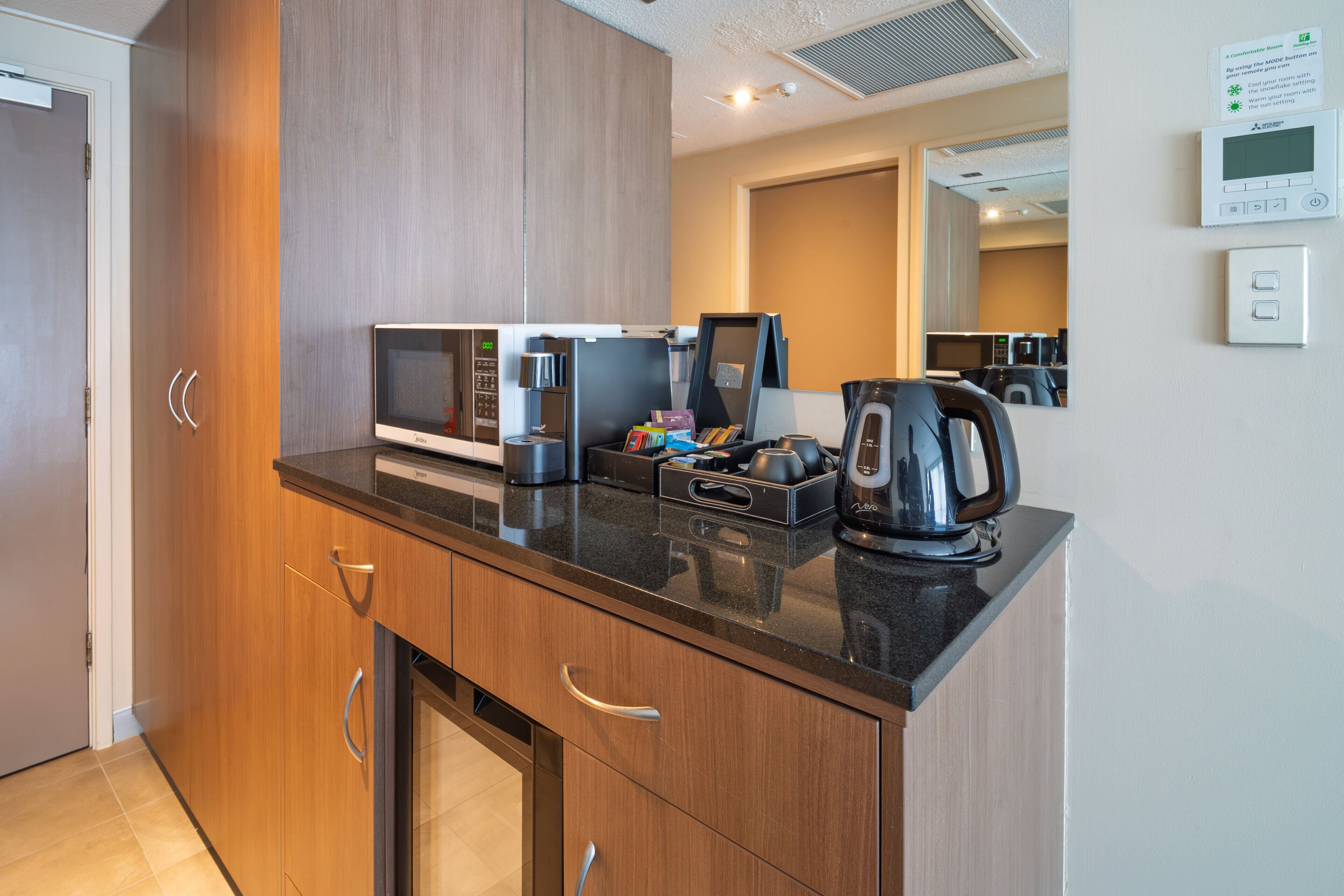 A modern kitchen with a microwave, coffee maker, and kettle on the counter, wooden cabinets, and a small refrigerator.