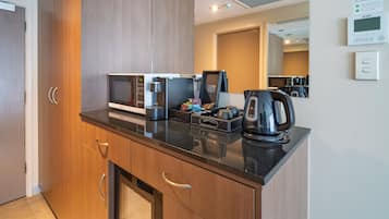 Una cocina moderna con microondas, cafetera y hervidor en la encimera, armarios de madera y un refrigerador pequeño.