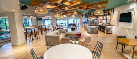 A modern interior with a central round table, multiple seating areas, and a kitchen area.