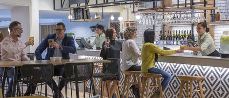 A modern bar area with wooden stools, a bar counter, and a variety of bottles and glasses on shelves.