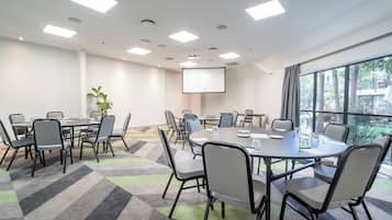 A conference room with multiple tables, chairs, a projector screen, and large windows.