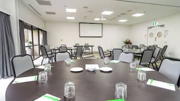 A conference room with a large table, chairs, a projector screen, and a window with curtains.