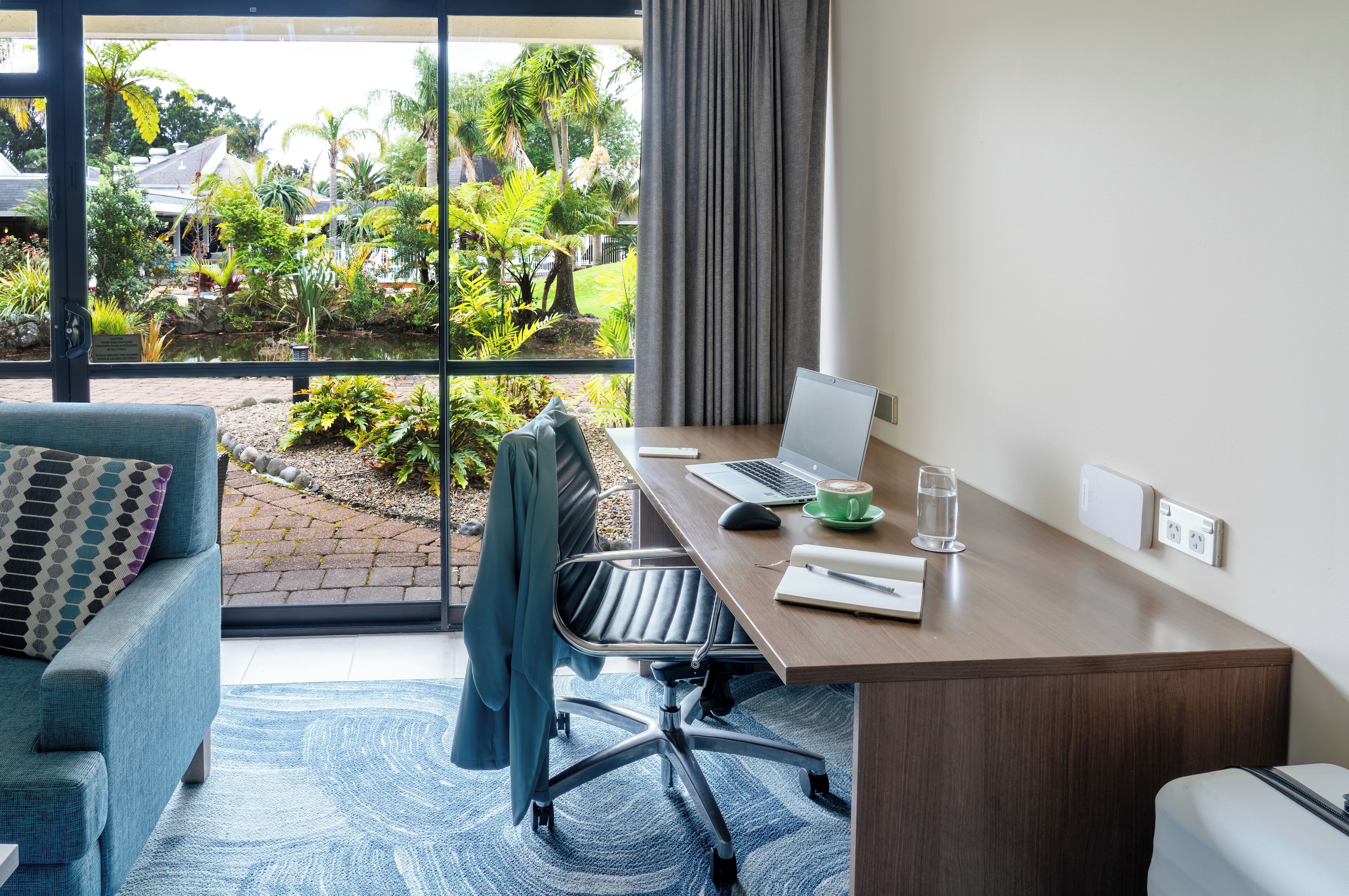 Une chambre d’hôtel moderne dotée d’une grande fenêtre, d’un bureau avec un ordinateur portable, d’une chaise et d’un canapé.