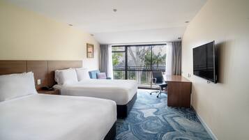 A hotel room with two beds, a desk, a chair, a TV, and a large window with a view.