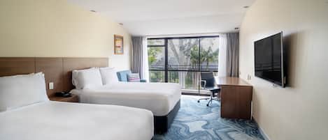 Habitación de hotel con dos camas, un escritorio, una silla, un televisor y un ventanal con vistas.