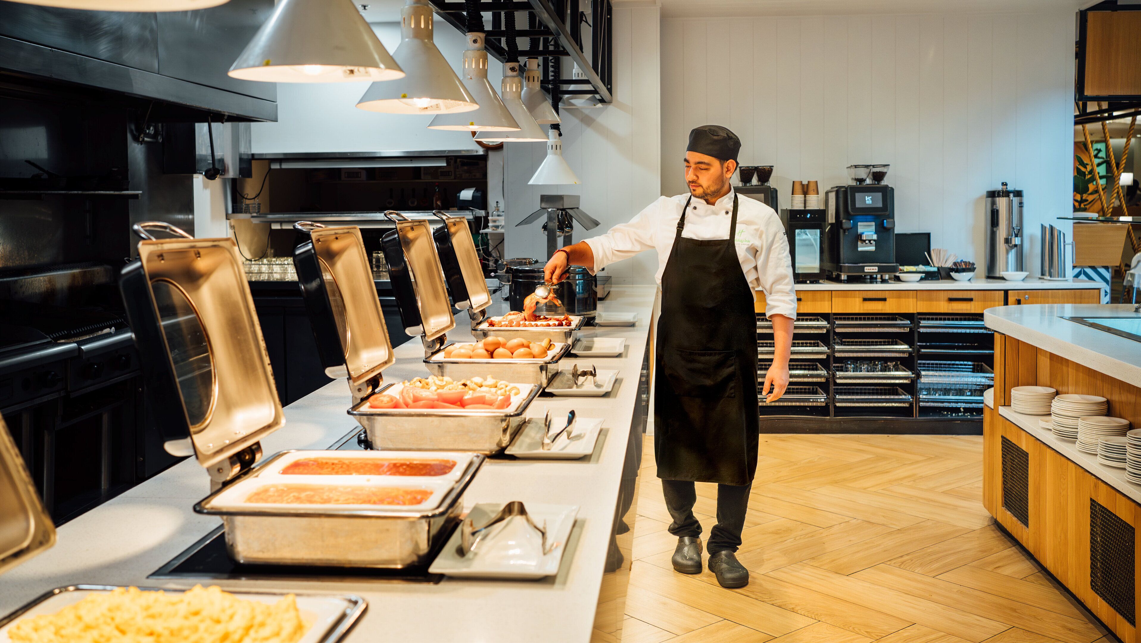 A buffet setup with multiple food stations, a chef serving food, and kitchen equipment in the background.
