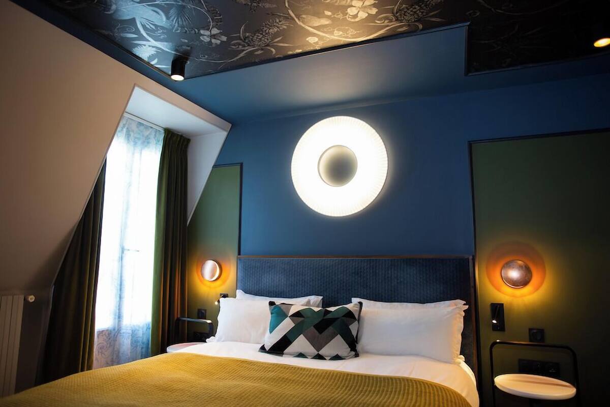 A modern hotel room with a large bed, two bedside lamps, and a circular wall light.