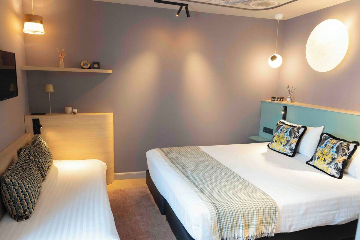 A hotel room with a bed, bedside tables, and a wall-mounted shelf with decorative items.