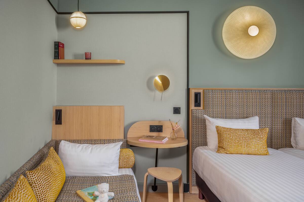 A hotel room with a bed, a sofa, a small table, and a wall-mounted shelf.