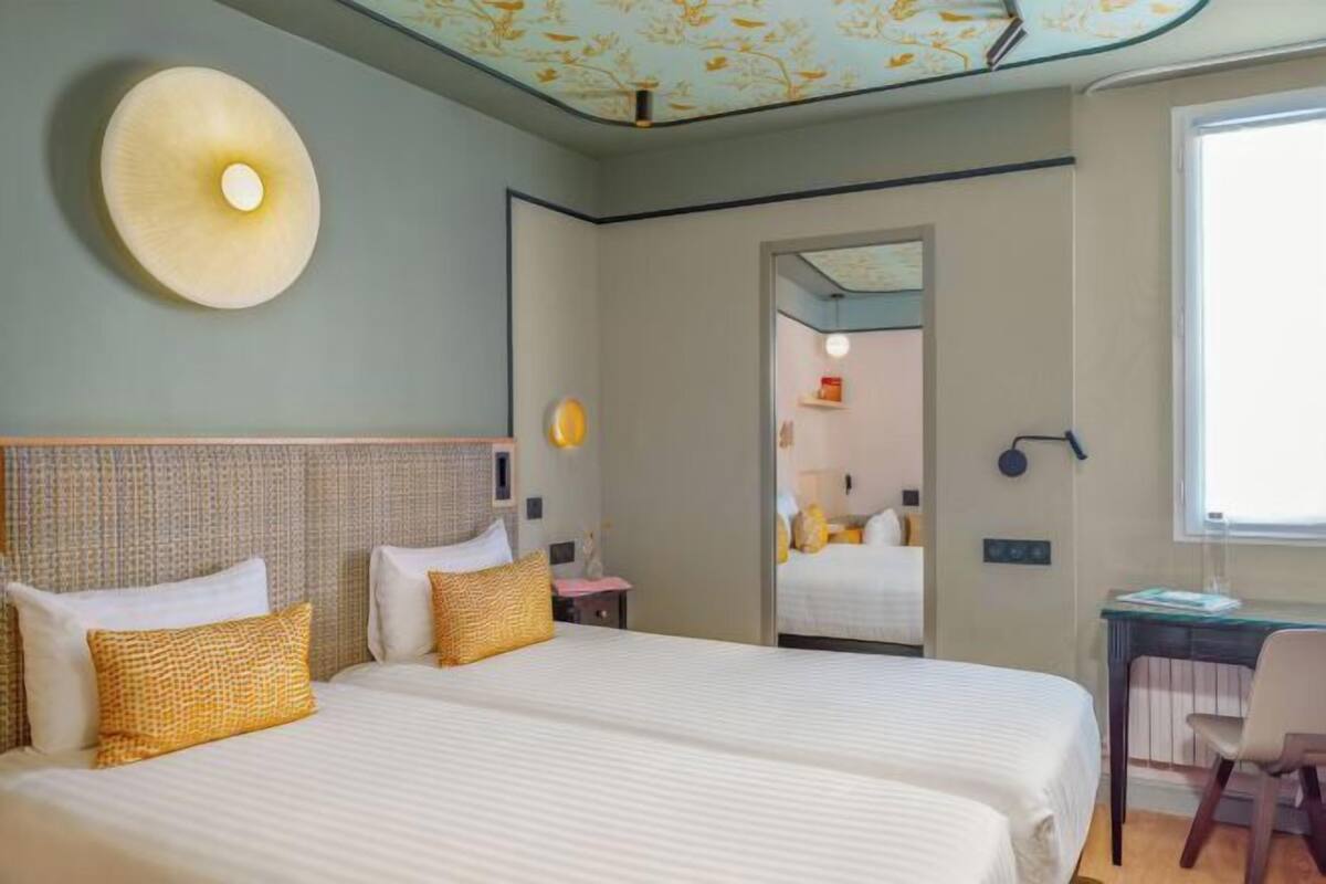 A hotel room with two beds, a desk, and a mirror.