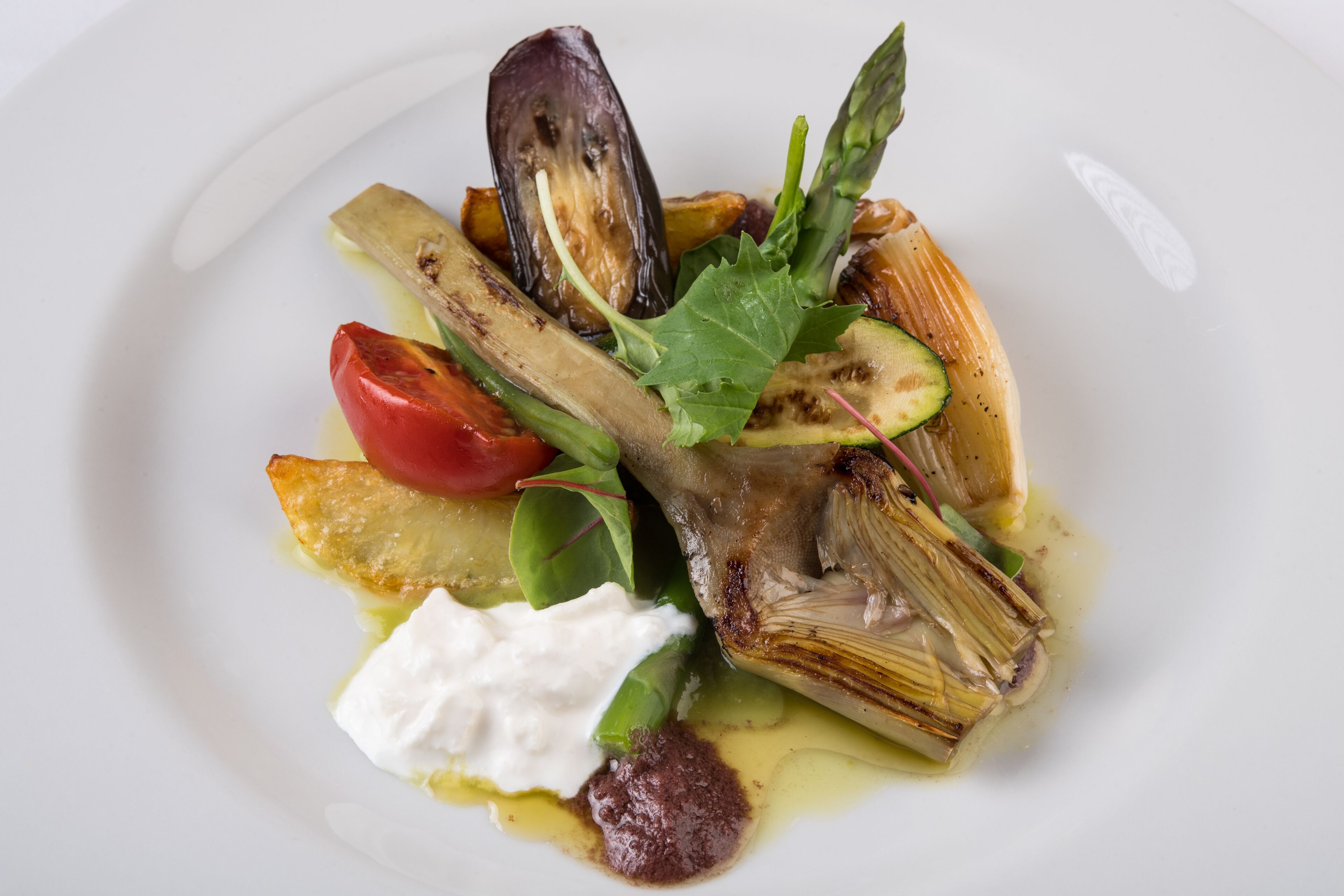 Un plato de comida con diferentes verduras y una cucharada de crema.