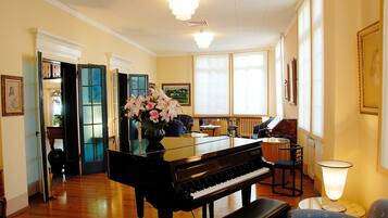 A grand piano in a spacious room with wooden floors, a comfortable seating area, and large windows allowing natural light.