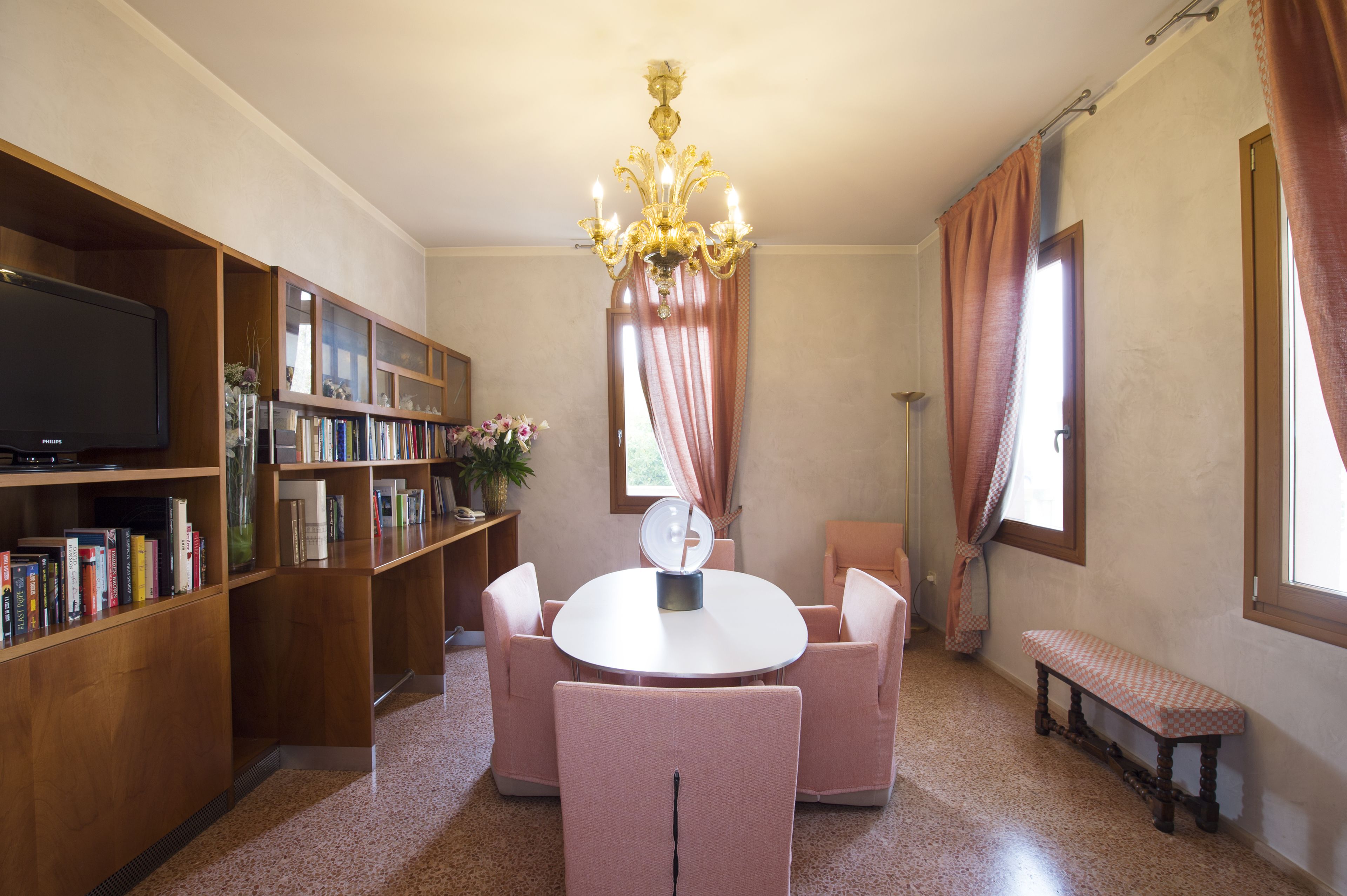 A library with a round table and chairs, bookshelves, a television, and a chandelier.