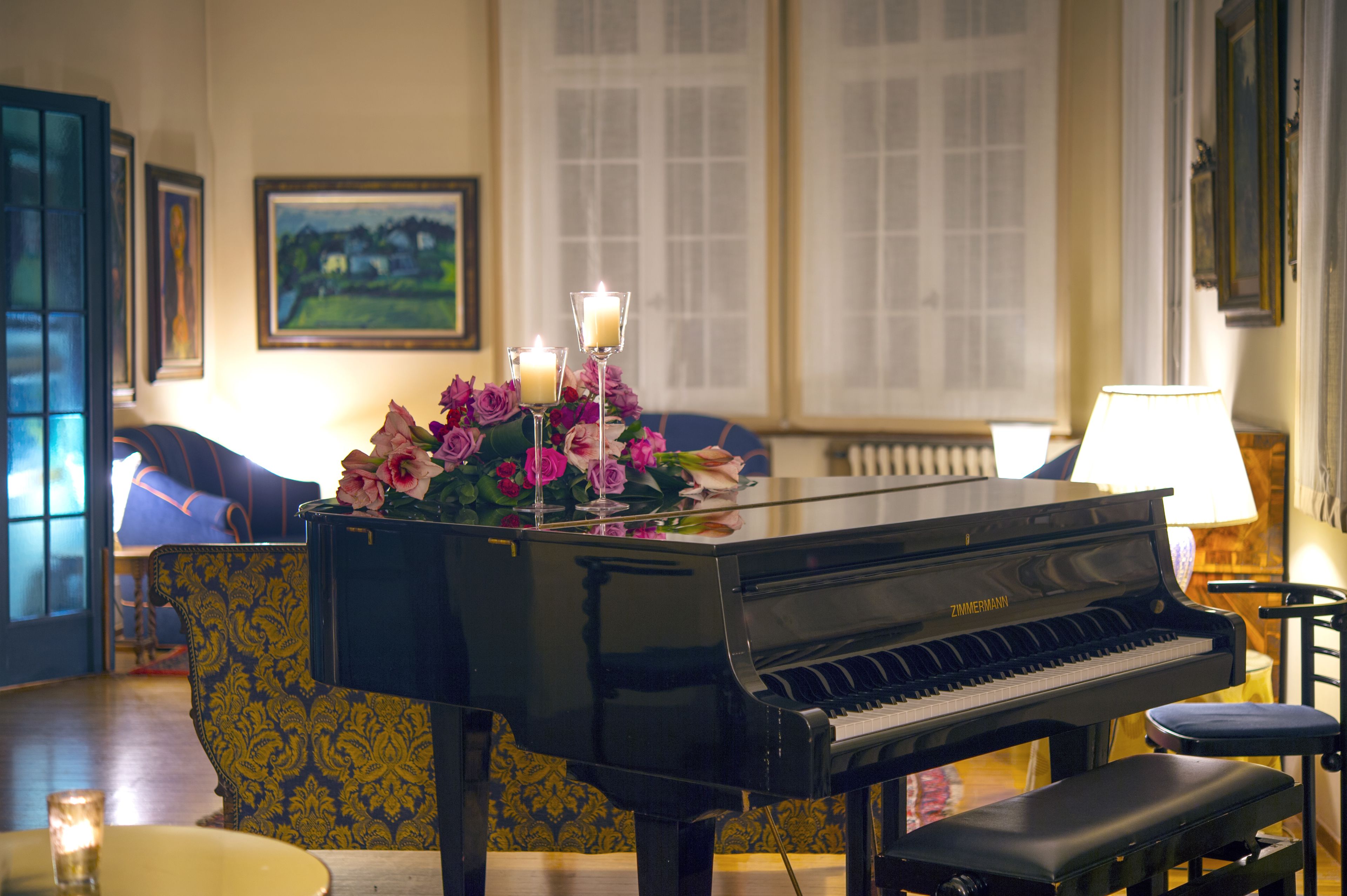 A grand piano in a room with a patterned armchair, a vase of flowers, and a lamp.