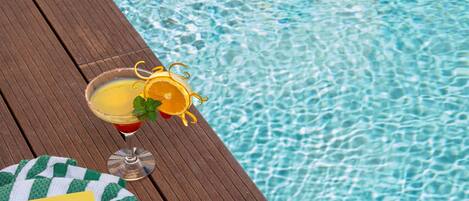 A wooden deck by a pool with a drink, a book, and a towel.