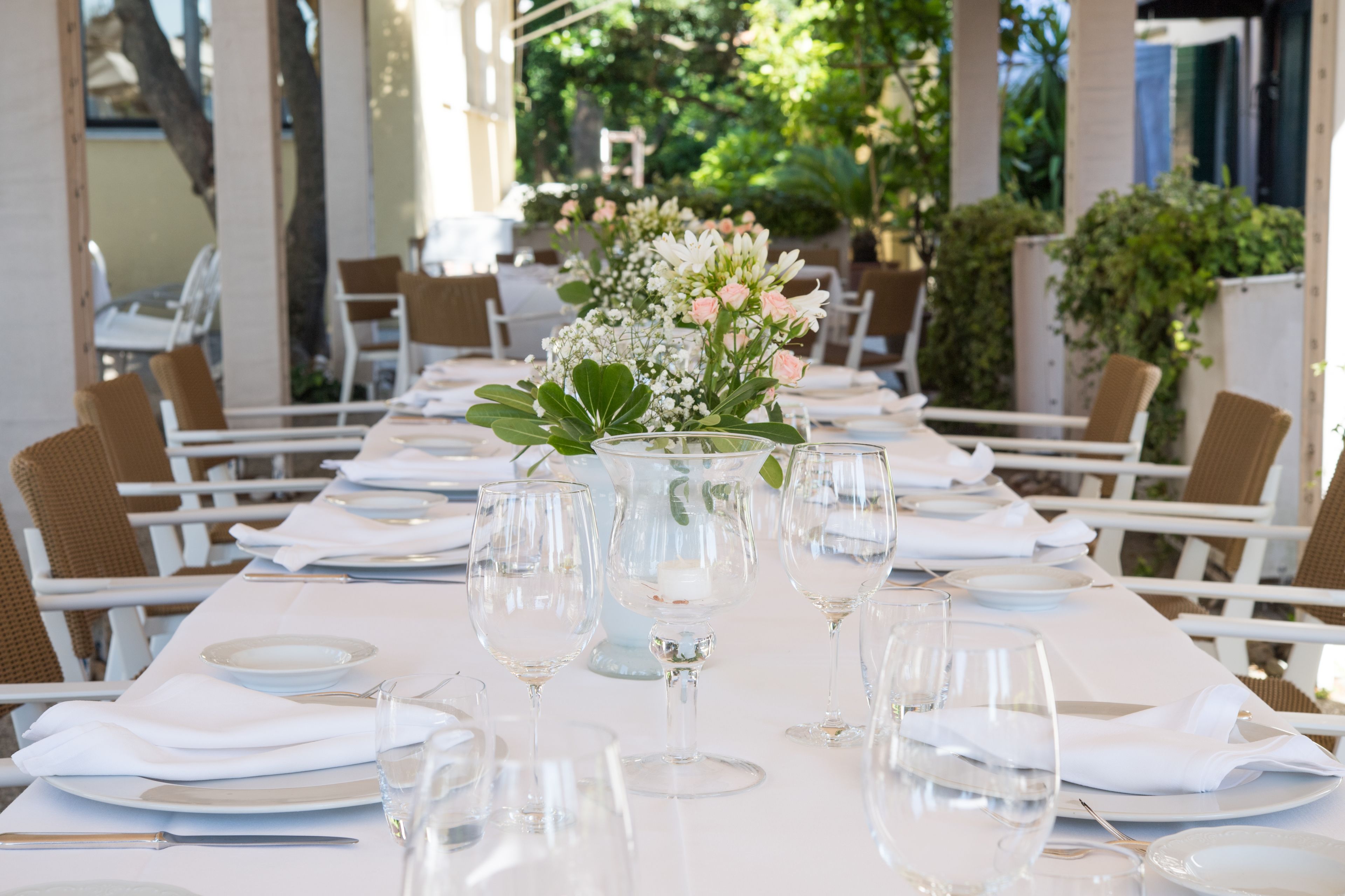 A restaurant table set with white tablecloths, clear glassware, and a centerpiece of flowers.