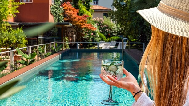 A person relaxing by a pool with a drink, surrounded by greenery and a building with balconies. - Hotel Villa Mabapa (Venice)