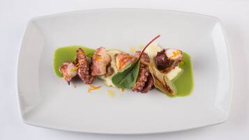 A white rectangular plate with octopus pieces, green sauce, and a garnish.
