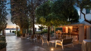 An outdoor seating area with chairs and tables, a bar, and a view of the water. - Hotel Villa Mabapa (Venice)