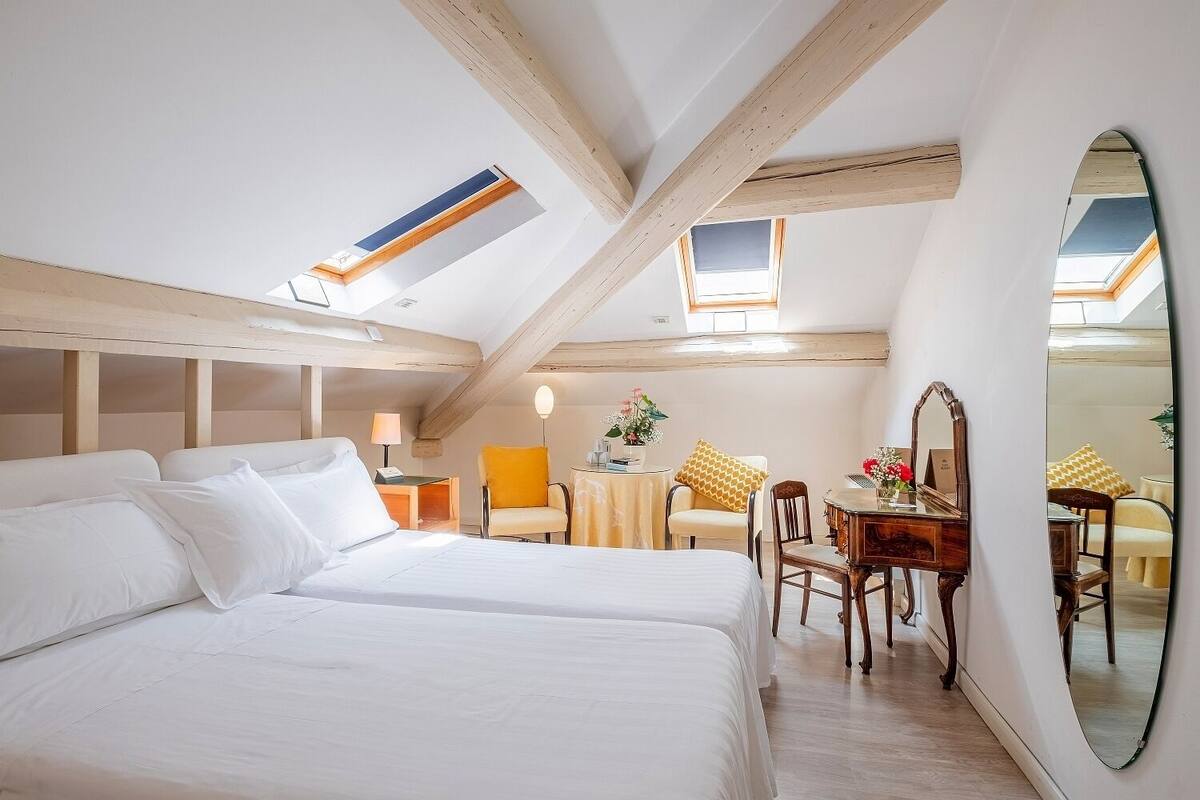 A bedroom with two beds, a small table with chairs, a mirror, and skylights.