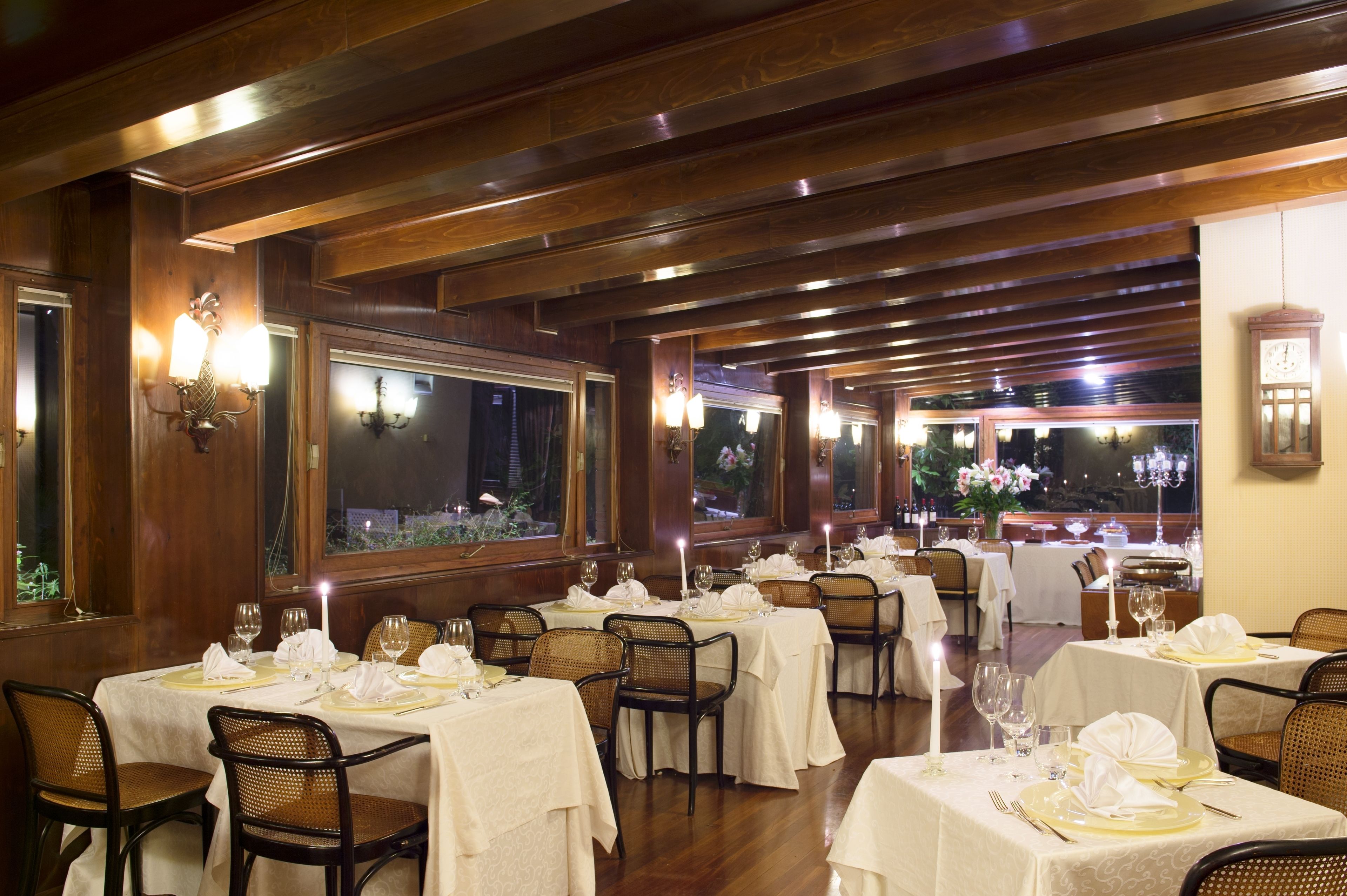 Un restaurant doté de nombreuses tables dressées pour le service, avec un décor comprenant des lambris en bois et de grandes fenêtres.