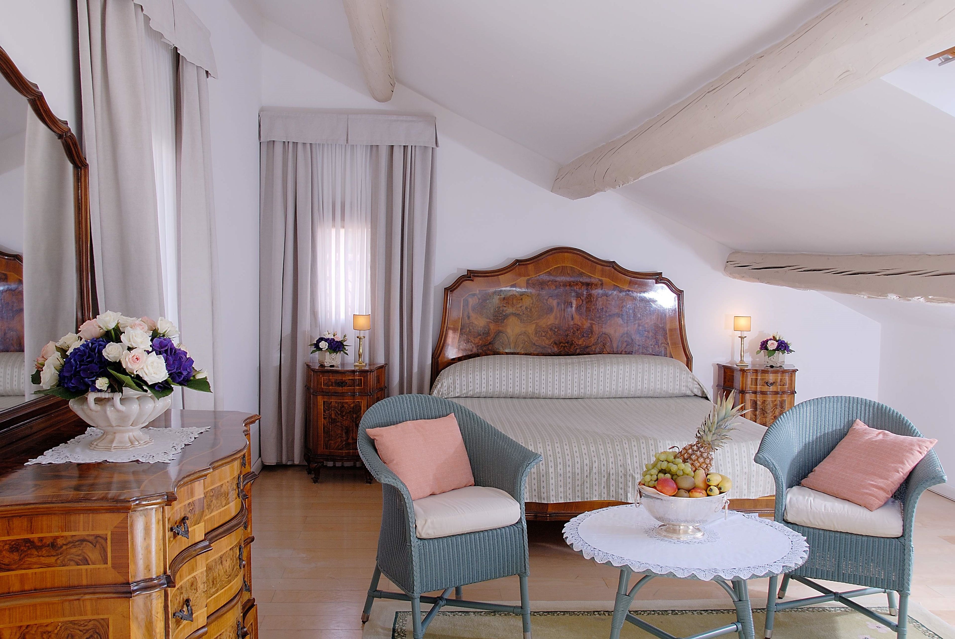 Un dormitorio con una cama grande, dos sillones, un aparador y una mesita de noche con una lámpara.