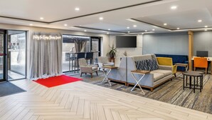 Eine moderne Hotellobby mit einem großzügigen Sitzbereich, einem roten Teppich und einem großen Fenster mit Vorhängen.