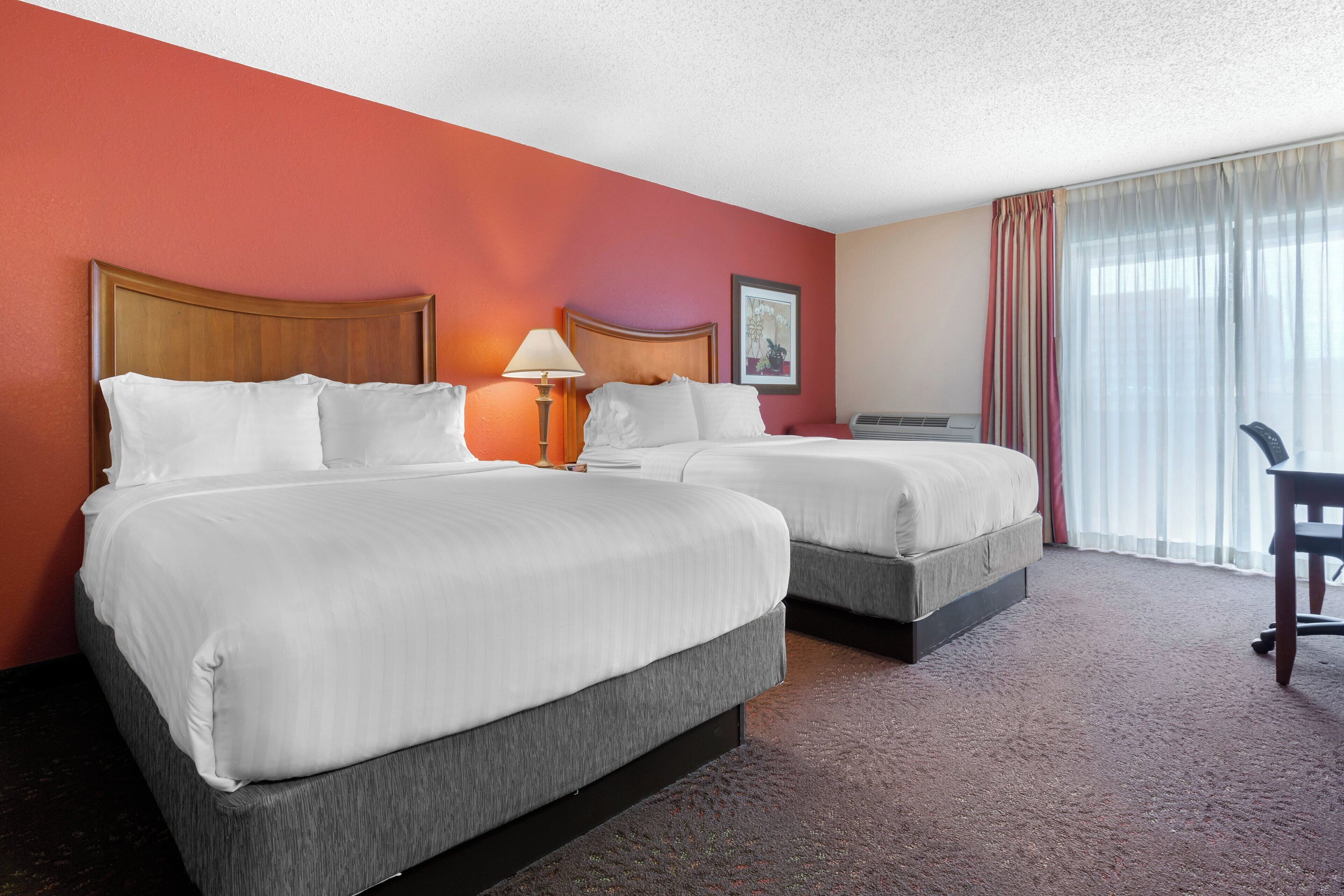 A hotel room with two beds, a desk, a chair, and a window with curtains.