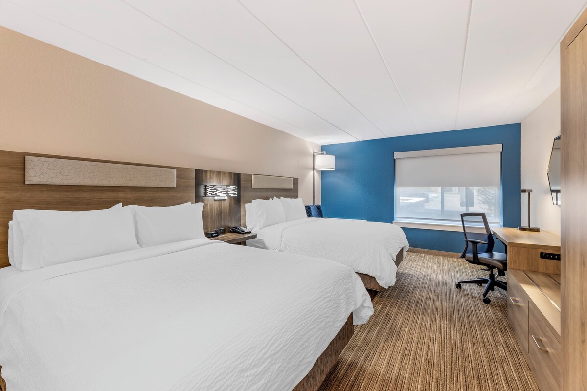 Habitació d'hotel amb dos llits, una taula de treball, una cadira, una làmpada i una finestra amb vistes.