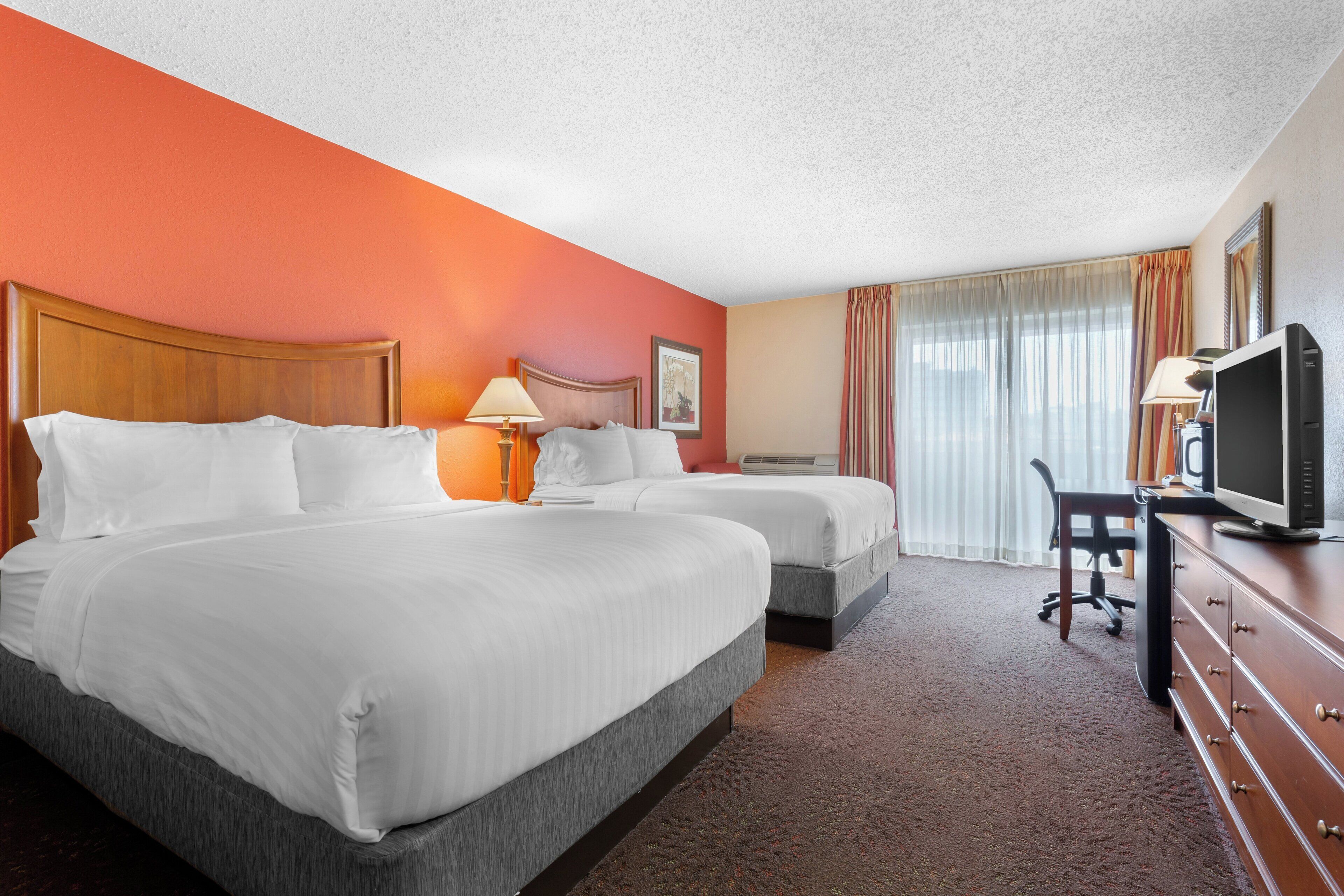 A hotel room with two beds, a desk with a television, and a window with curtains.