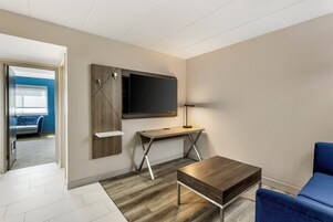Una habitación de hotel moderna con un escritorio de madera, un televisor de pantalla plana, una lámpara y una silla azul.