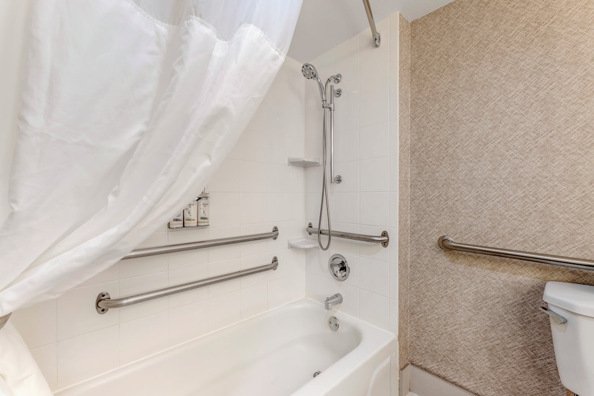 A bathroom with a bathtub, a shower, and a toilet. There are grab bars installed for safety.