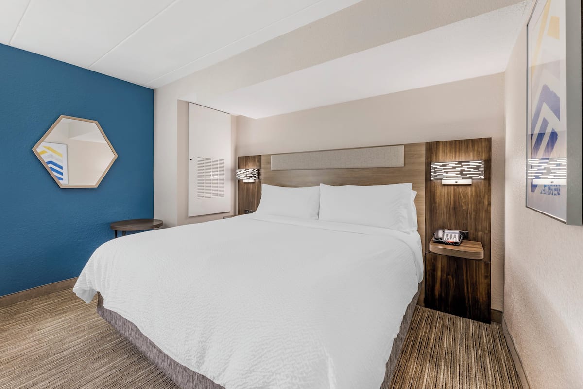A hotel room with a large bed, a wooden headboard, a bedside table with a phone, and a blue accent wall.