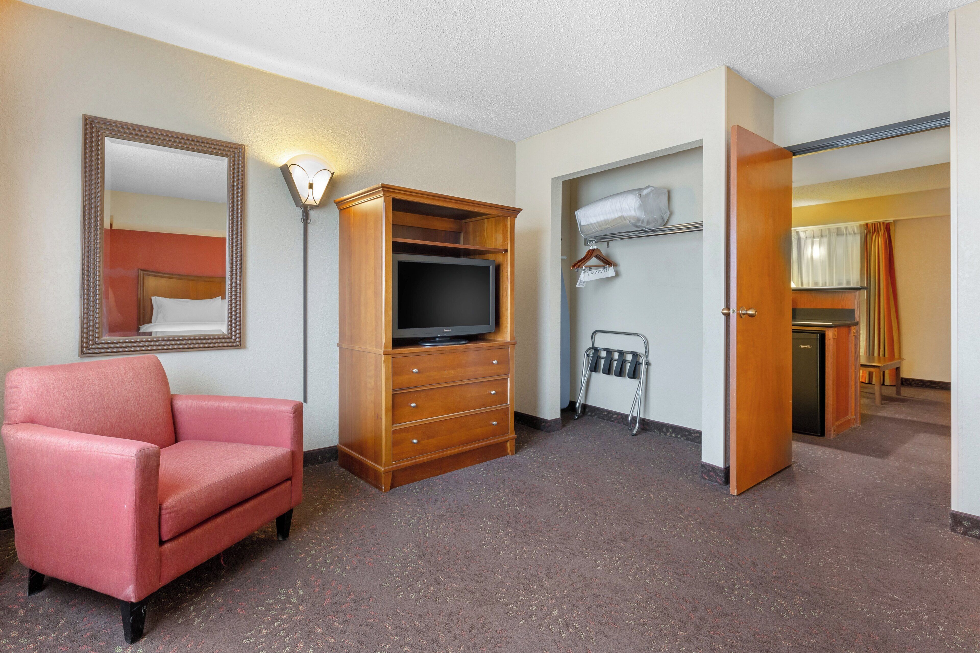 Una habitación de hotel con televisión, cómoda, una silla rosa y espejo.