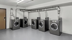 A laundry facility with four washing machines, a ventilation system, and a door. - Red Roof Inn Perryville (Perryville)