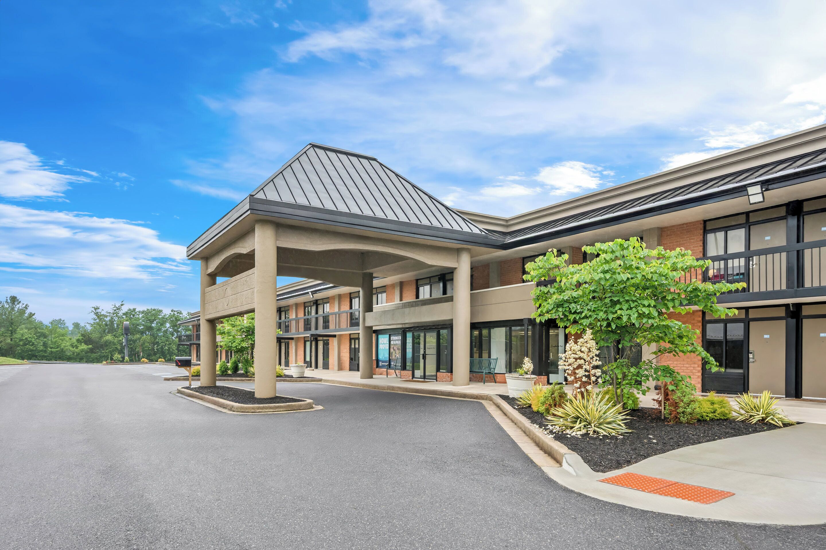A modern building with a covered entrance, large windows, and a landscaped area with plants.