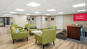 A modern lounge area with green armchairs, a wooden table, and a red sign indicating free Wi-Fi in all rooms. - Red Roof Inn Perryville (Perryville)