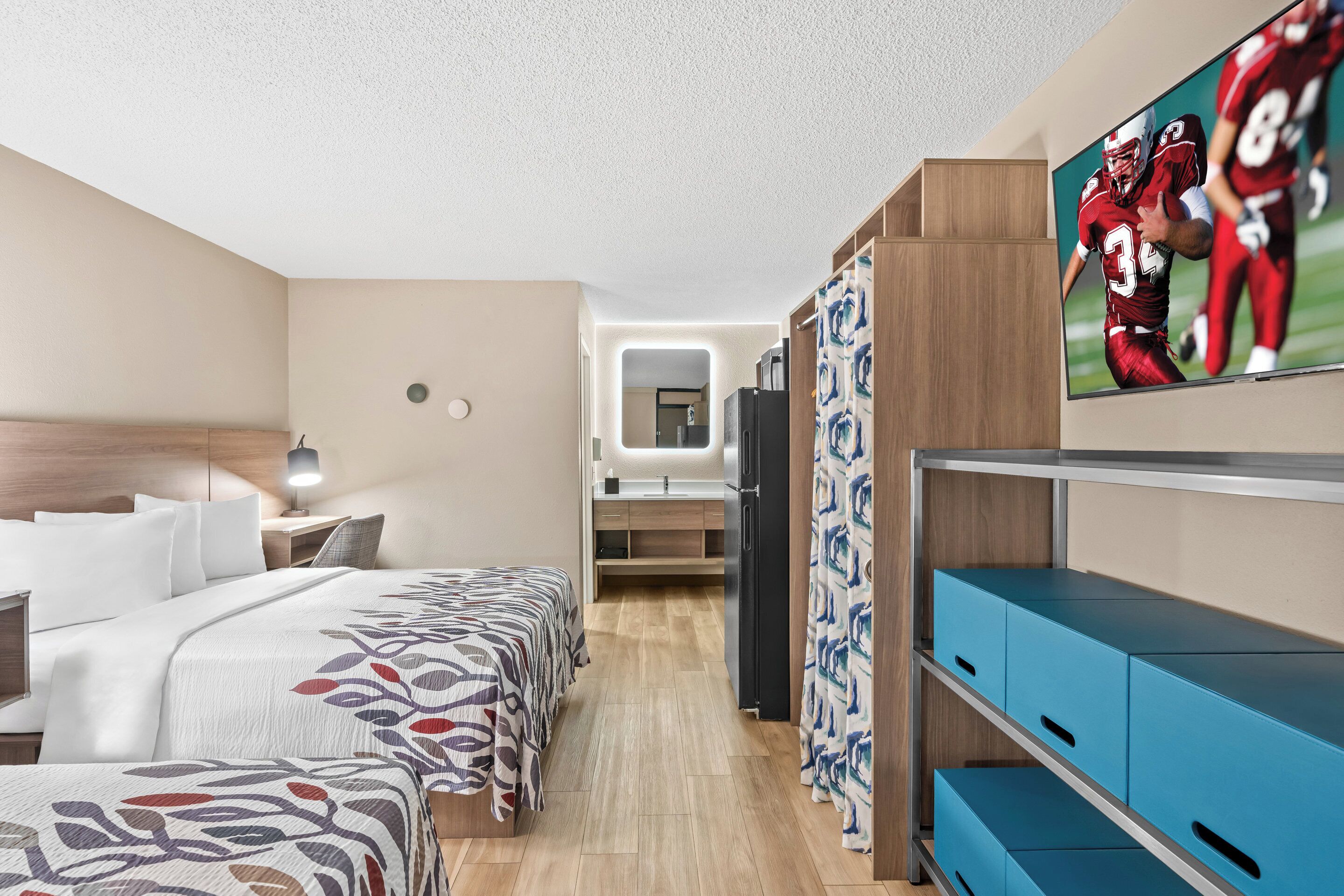 A hotel room with a bed, bedside table, lamp, TV, wardrobe, and a mirror.