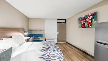 A hotel room with a bed, a desk, a chair, a TV, and a refrigerator.