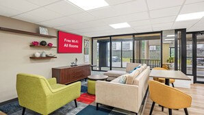 A modern lounge area with a sofa, armchairs, a small table, and a TV screen advertising free Wi-Fi. - Red Roof Inn Perryville (Perryville)
