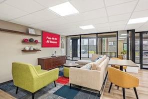 A modern lounge area with a sofa, armchairs, a small table, and a TV screen advertising free Wi-Fi. - Red Roof Inn Perryville (Perryville)